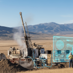 Geothermal drilling rig in a dry, mountainous U.S. landscape with engineers interacting with a holographic AI interface.