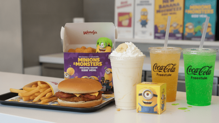 A Wendy's tray with a burger, fries, chicken nuggets, two drinks, a frosty, and Minions toys on a counter.