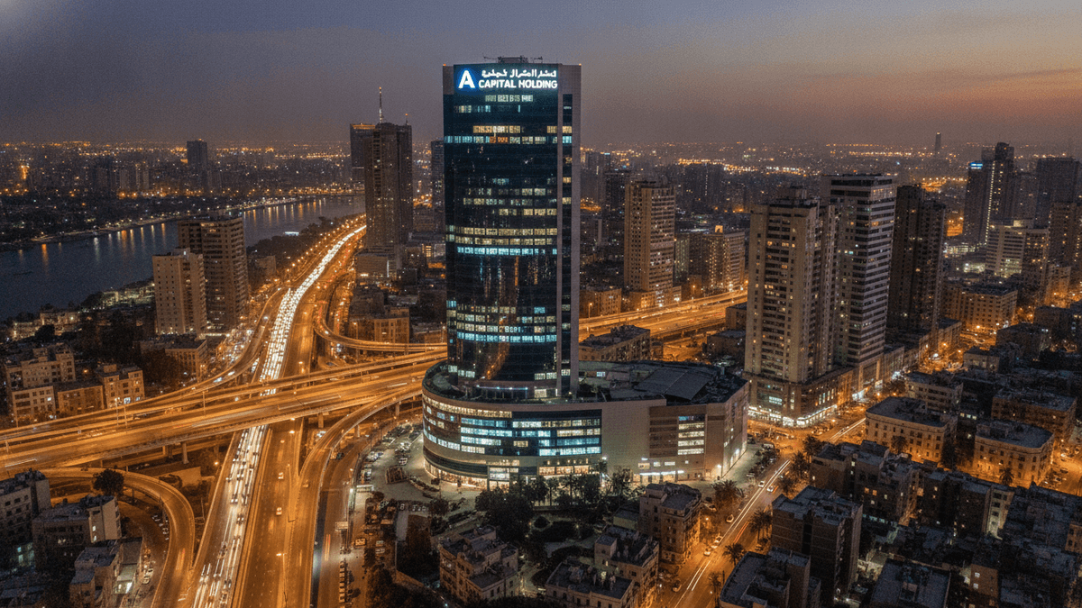 An aerial view of a modern skyscraper with "A CAPITAL HOLDING" illuminated at its top, surrounded by city lights and a river at dusk.