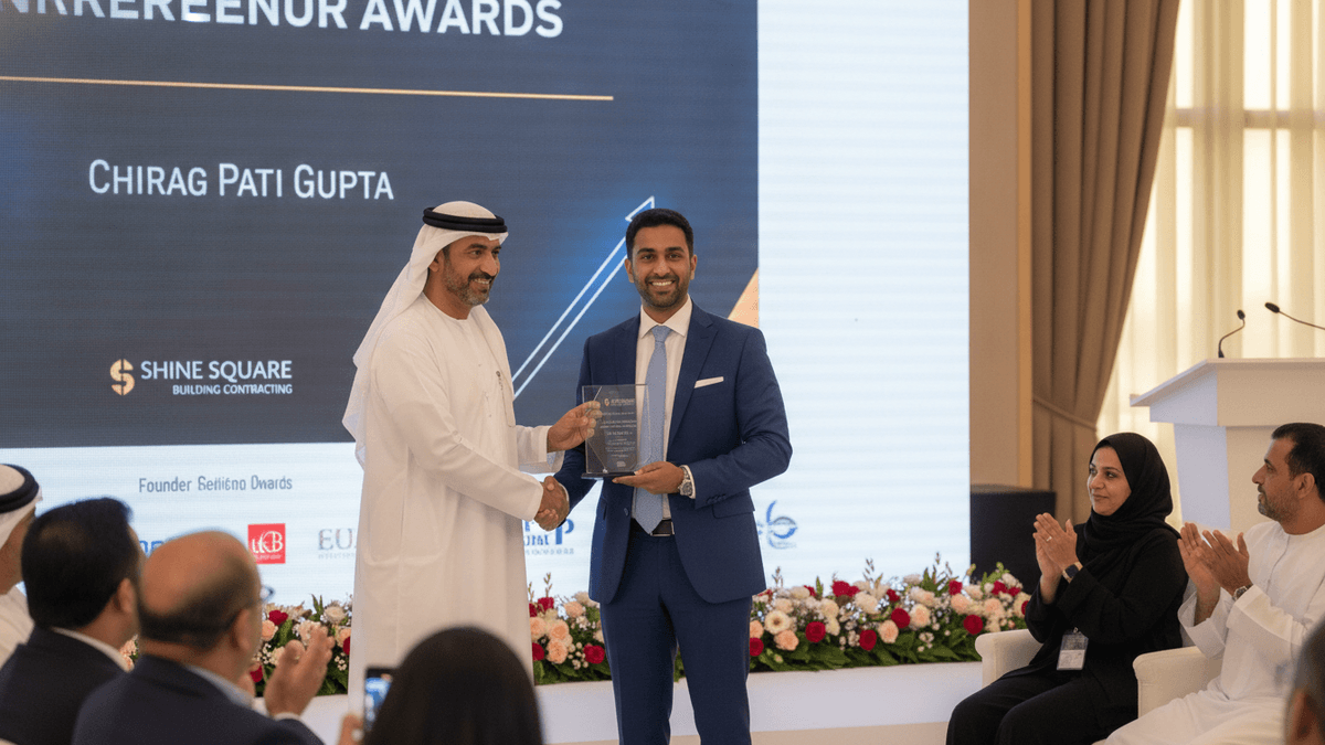 Chirag Pati Gupta, in a blue suit, shakes hands with an Omani dignitary in white robes, receiving an award plaque on a stage.