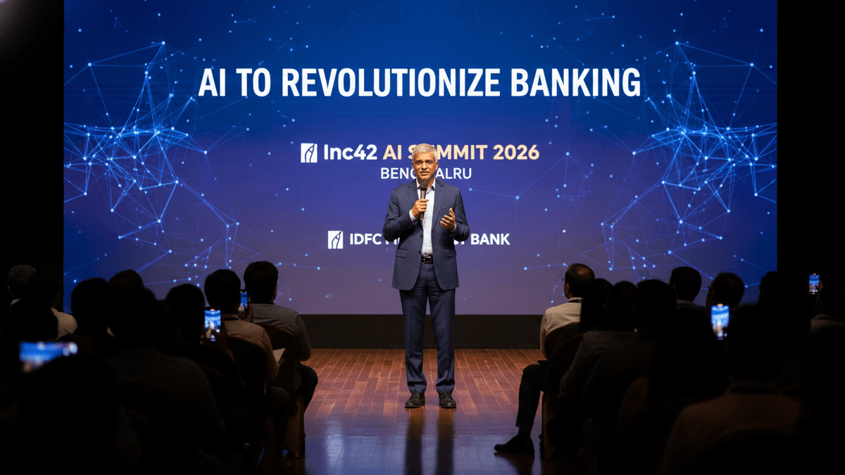 A man in a suit speaks on a stage with a large screen behind him displaying "AI TO REVOLUTIONIZE BANKING."