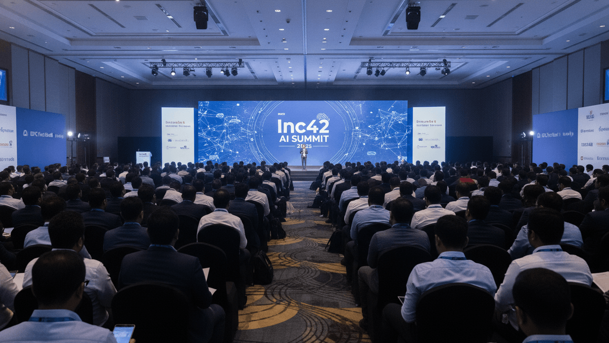 A wide shot of a large conference hall with an audience seated, facing a brightly lit stage with a large screen displaying "Inc42 AI Summit."