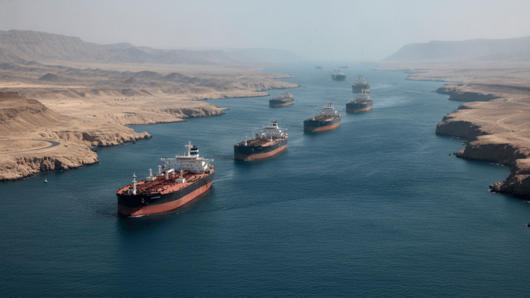 An aerial view of multiple large crude oil tankers navigating a narrow strait between arid landmasses.
