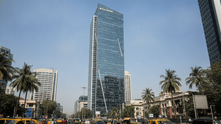A modern, glass-clad skyscraper with "AXIS BANK" at the top, towering over a busy street in an Indian city with palm trees.