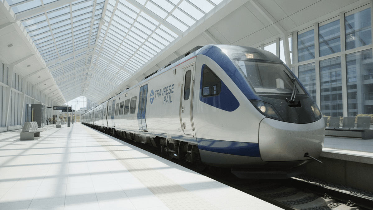 A modern silver and blue train with TRAVESE RAIL branding is parked at a clean, well-lit station platform.
