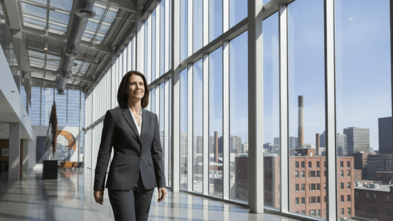 An individual investor stands in a sunlit financial lobby, looking out at a city skyline with industrial buildings.