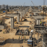 An elevated view of a large elevated highway construction site in India with numerous workers and heavy machinery.