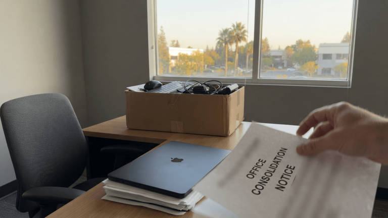 A cardboard box and a laptop on a desk in a quiet office, symbolizing the closure of a technical hub.
